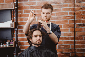Barber shop, warm toning photo. Man in barbershop chair, hairdresser styling his long hair