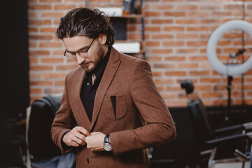 Concept status men client in barbershop. Portrait stylish man in jacket and glasses against background of barber chair in hairdresser.