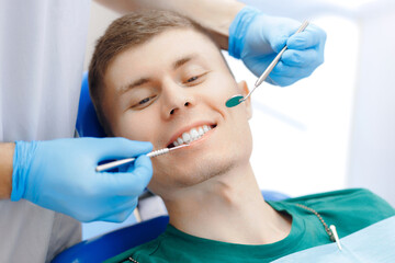 Young man getting dental checkup in Dentistry clinic. Dentist using equipment probe and mirror for examination of teeth of man patient