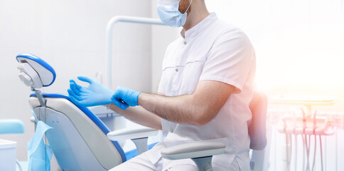 Banner dentistry, professional dentist puts on blue medical gloves in dental office - obrazy, fototapety, plakaty