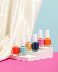 set of colorful nail polishes on stair podium with silky fabric and blue and pink background