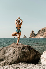 Yoga on the beach. A happy woman meditating in a yoga pose on the beach, surrounded by the ocean and rock mountains, promoting a healthy lifestyle outdoors in nature, and inspiring fitness concept.