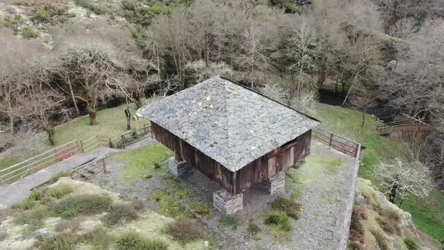 Aerial view of a traditional Asturian h&oacute;rreo with a stone base and moss-covered roof, surrounded by a rustic wooden fence in a rural landscape