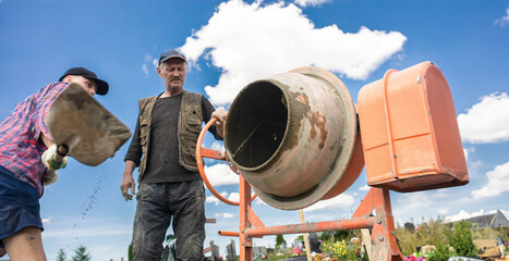 concrete mixer and a male worker working during the day in the summer.