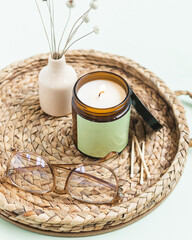 Green candle in amber jar burning on woven tray