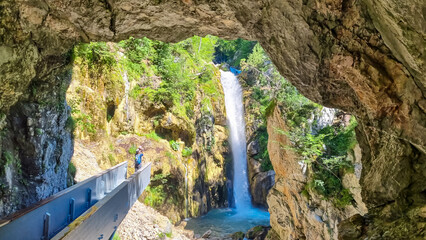 Man on viewing platform with scenic view of Tschaukofall, Tscheppaschlucht, Loibl Valley, Karawanks, Carinthia, Austria. Water cascading from cliff creating misty spray. Narrow gorge in remote canyon