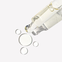 Clear serum in glass dropper with texture drops on white background