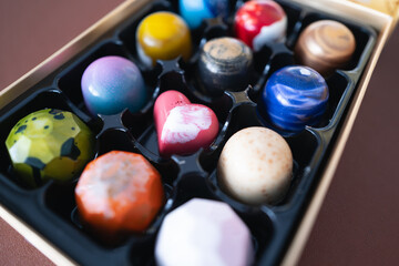 A hearth shaped chocolate in a box of colourful hand crafted artisan treats in a presentation box. They have  smooth shells with pretty patterns. - 698709298
