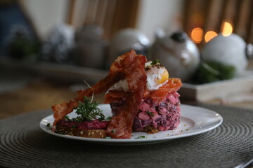 Breakfast arrangement with salmon tartar, poached egg and fried bacon in living room