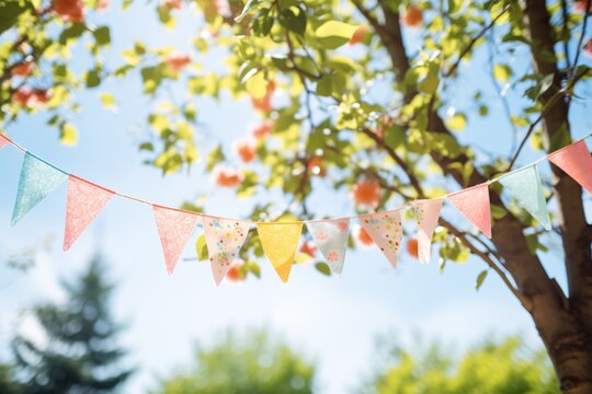 Vibrant bunting garland in verdant tree leaves against azure sky, summer celebration design with room for text.