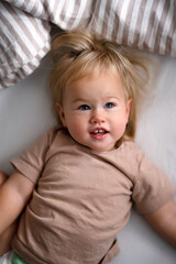 Cute caucasian blonde baby child on white sheets on the bed