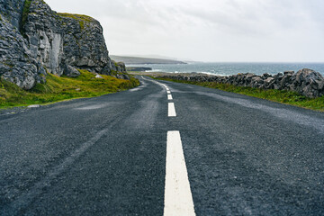 Authentic Irish landscape in County Clare with lonely road with dashed lines and sea in the...