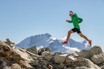 Runner in a green jacket leaping between rocks in high altitude