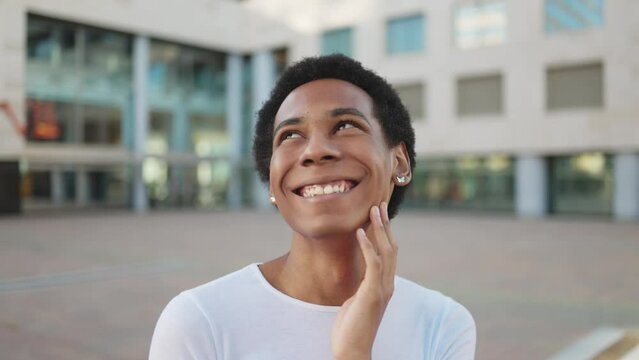 Cheerful African American non-binary person laughing in city street. Portrait of a happy transgender afro person with very short hair smiling. Concept of LGBT diversity and inclusion. Gender equality