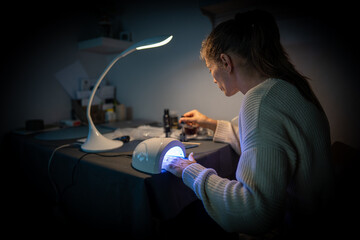 Attractive woman doing herself a manicure at home in the evening in a dark room