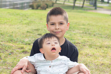 Boy with his brother with down syndrome sitting on the grass in a park