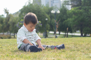 White boy with down syndrome sitting on the grass playing in a park