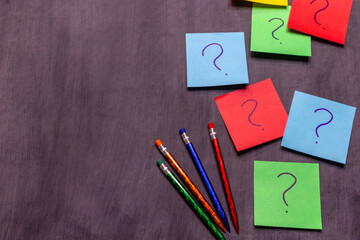Multicolor note pads with question marks and pencils on gray background with copy space