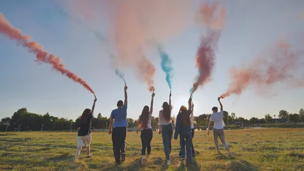 Fotobehang A group of friends spraying multi-colored smoke at sunset. © Довидович Михаил