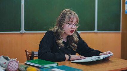 A schoolgirl in the role of a teacher sits at her desk.