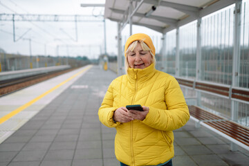 Portrait of 50s senior woman using mobile phone while waiting on tram station. . High quality photo