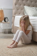 Little girl sitting in the bedroom, crying and covering face with hands