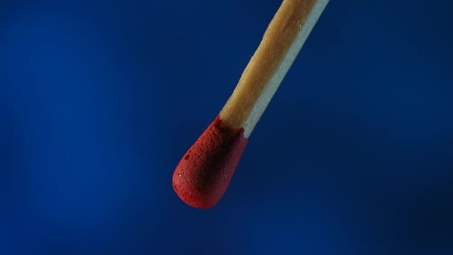 Macro video captures the moment of ignition of the match and its flame on a blue background. From the flare up to the bright burning. The red sulfur of the match flashes fire and the wood burns.