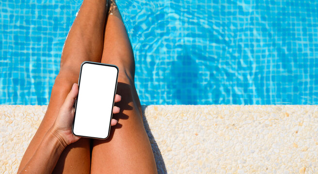 The phone is on the legs of a girl by the pool. Close-up. phone with blank white display. girl on summer vacation.
