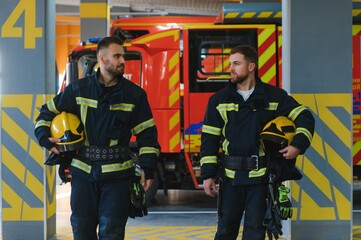 Two firefighters in protective clothing in helmets with fire engine