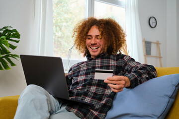 Latin young man buying online with a credit card in his laptop at home. Black Friday sales. - obrazy, fototapety, plakaty