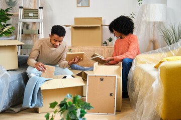 Young black couple packing in a moving cardboard boxes to settle in a new home. New residence...