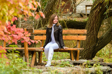 A young beautiful girl sits on a bench in an autumn park and looks at the surrounding nature