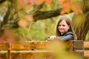 A young beautiful girl sits on a bench in an autumn park and turns around and looks into the frame.