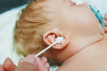 Cute little caucasian baby boy looking at camera while ear cleaning by his parent. Happy baby...