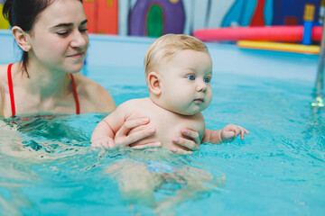 Fototapeta na wymiar A 5-month-old baby learns to swim in a pool with a coach. Baby learning to swim.
