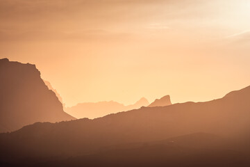 Italian Dolomites in colorful golden sunrise. Misty Alpine mountains in haze. Silhouettes of mountain peaks. 