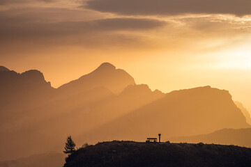 Italian Dolomites in colorful golden sunrise. Misty Alpine mountains in haze. Silhouettes of mountain peaks. 