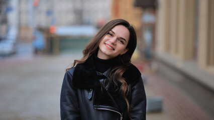 Happy brunette girl posing in black jacket in autumn in the city.