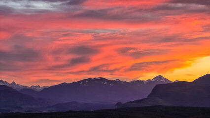 Scenic view of snow capped mountain peak Dobratsch at sunset seen from Taborhoehe in Carinthia, Austria, Europe. Sky has vibrant orange and pink colors with clouds swirling around summit. Serenity