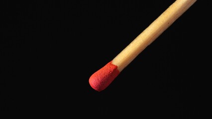 A macro shot of a matchstick against a black background. A wooden match with red sulfur.