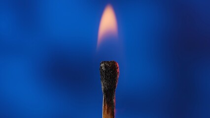Macro shot of a burning match against a blue studio background. The flame of the burning match...