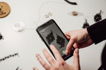 Creative jewellery artist is taking photo of handmade earrings with smartphone.