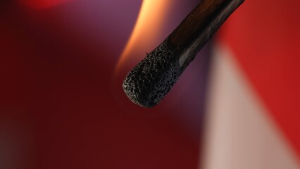 Macro shot of a burning match against a red studio background. The flame of the burning match...