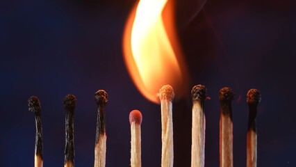 A row of matches where two burning matches pass their fire to the next. Cascade of flame, transfer of energy. Macro shot of the transition of flame from one match to another. - obrazy, fototapety, plakaty