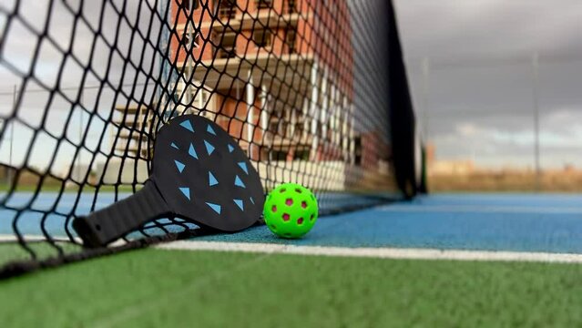 video of pickleball ball and paddles resting on the net of a pickleball court