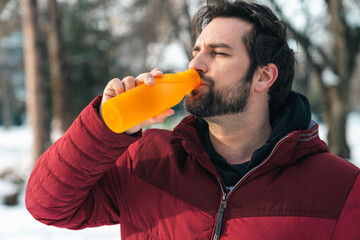 Closeup of man in red jacket drinking water from water bottle standing outdoors in winter.