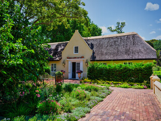 Fototapeta na wymiar Cape Dutch building and brick walkway surrounded by lush garden at Vergelegen Wine Estate, Somerset West, South Africa