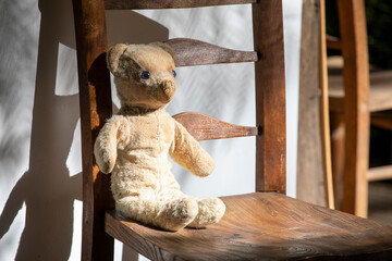 Old worn Teddy bear on a wooden chair outside with shadows.