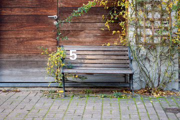 A bench placed on the sidewalk, a wooden bench with the number 5