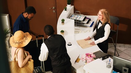 People arriving at hotel front desk, preparing to do check in at reception counter and see room...